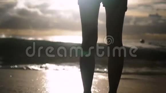 穿短裤的年轻女子独自站在夕阳下的海滩上视频的预览图