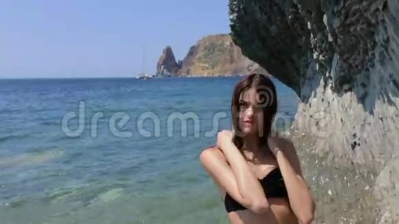 一个皮肤棕发的长头发身穿黑色泳衣站在岩石附近的海面上摆着姿势视频的预览图