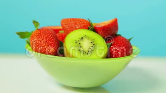 绿色盘子上蓝色背景的鲜奇异果和草莓片旋转成一个圆圈视频的预览图