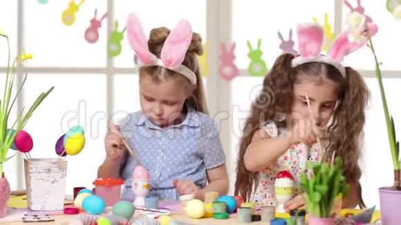快乐的孩子们在复活节穿着兔子耳朵画鸡蛋视频的预览图