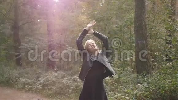 女孩在秋天缓慢地抛着手臂微笑着走进镜头在森林里摆着时尚的姿势视频的预览图