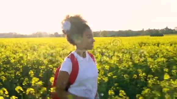 混血儿非裔美国少女女青年带着红色背包和一瓶水在花田徒步旅行视频的预览图