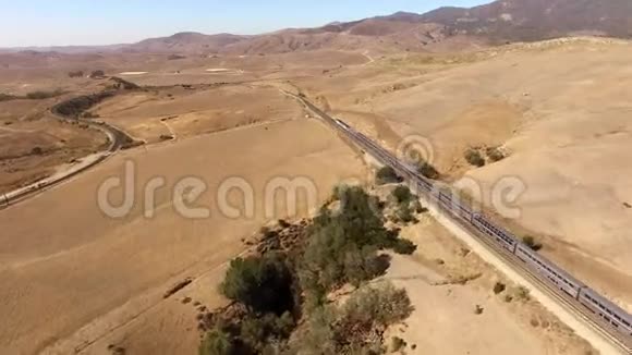 4k空中无人机大型现代化城市客运列车在沙质草原景观中穿越干燥沙漠峡谷的全景图视频的预览图