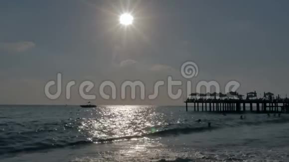 夕阳下的卵石沙滩上有漂浮的人在海边码头附近有巨浪视频的预览图