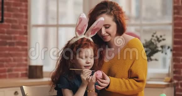 复活节快乐妈妈教女儿画鸡蛋为复活节做准备的幸福家庭他们戴着兔子耳朵视频的预览图