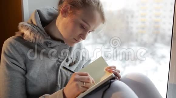 年轻女孩坐在一扇大窗户上写日记视频的预览图