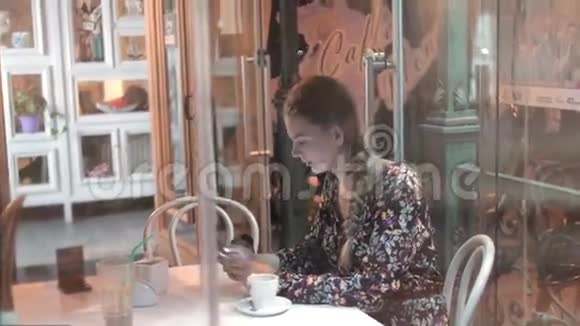 通过咖啡屋窗口观看与城市倒影的女人正在使用手机智能手机的年轻学生视频的预览图