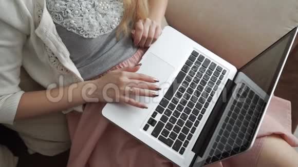 年轻女子坐在沙发上用笔记本电脑和微笑双手特写键盘上的手指视频的预览图