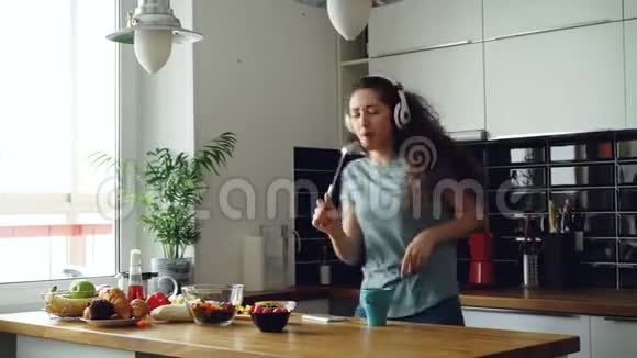 快乐的年轻有趣的女人在家里的厨房里悠闲地跳舞唱歌视频的预览图