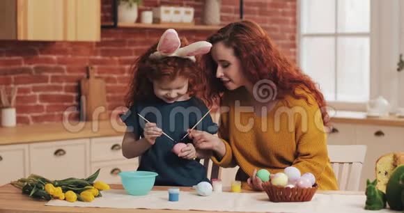 复活节快乐妈妈教女儿画鸡蛋为复活节做准备的幸福家庭小女孩戴着兔耳朵视频的预览图