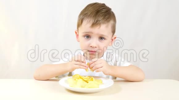 小男孩正坐在白色背景的桌子旁吃薯片视频的预览图