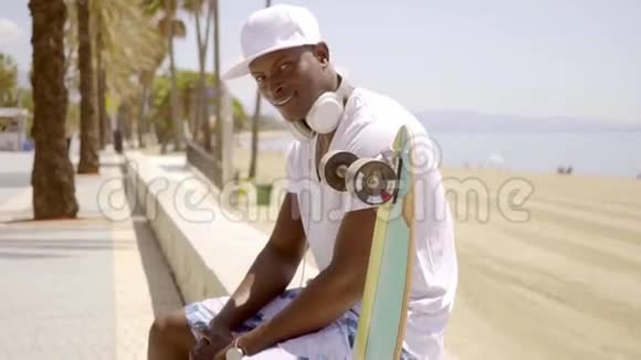 坐在沙滩墙上的英俊的年轻黑人视频的预览图