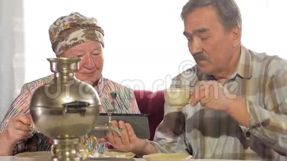 一对年长的夫妇喝着一个老式俄罗斯茶壶的茶在平板电脑上看了一张照片有胡子的人视频的预览图