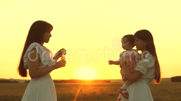 快乐的妈妈和孩子们一起吹肥皂泡日落时分女儿和母亲在公园里吹泡泡视频的预览图