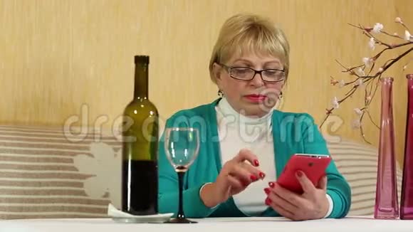 女人坐在桌边喝着红酒在智能手机上说话视频的预览图