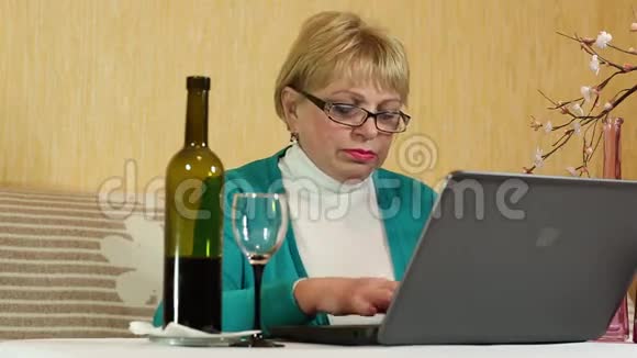 女人端着一瓶酒坐在桌边用笔记本打字视频的预览图