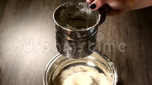 在家中的厨房里用金属碗中的筛杯特写一只雌性手筛面粉烹饪家庭烘焙视频的预览图