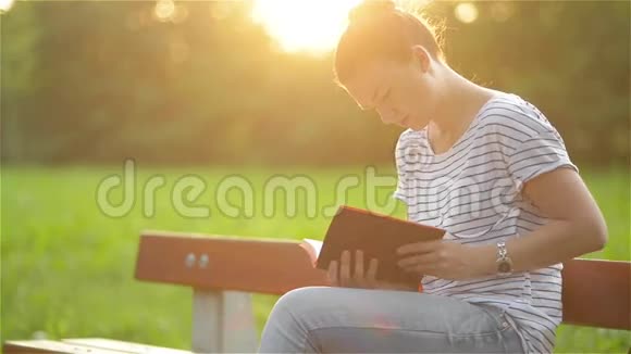 美丽的女人坐在公园的长凳上看书学生在花园里准备考试年轻的视频的预览图