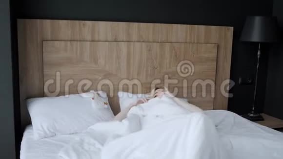 早上在酒店房间年轻女子坐在舒适的床上戴着面具睡在头上摩天大楼的窗户视频的预览图