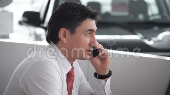 英俊的汽车推销员在展厅里打电话视频的预览图