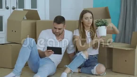 年轻夫妇在他们的新家里喝过汤后用平板电脑坐在地板上视频的预览图