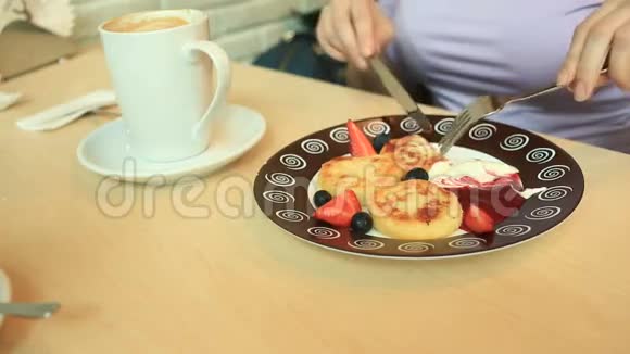 咖啡馆里的一个女孩吃奶酪煎饼里面有酸奶油果酱和新鲜浆果还有刀叉视频的预览图