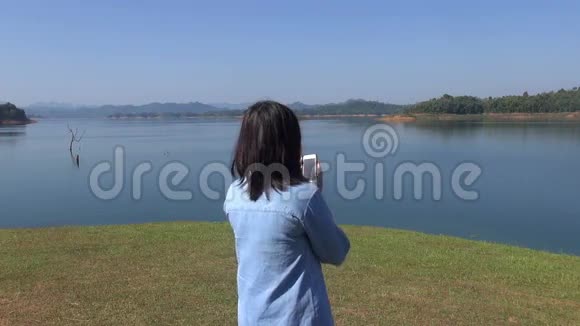女青年在湖边拍摄森林山美景视频的预览图