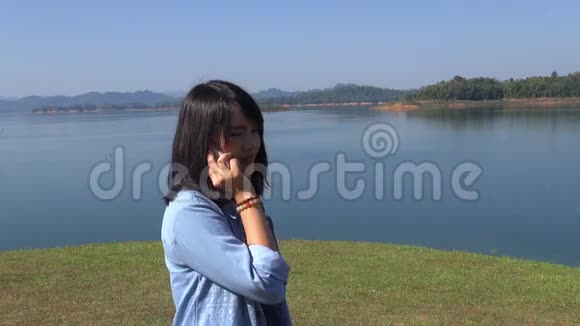 可爱的年轻女子在山前湖边打电话微笑视频的预览图
