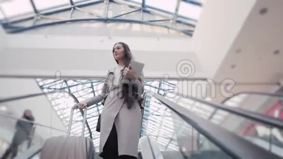 一个自信的女商人站在机场的自动扶梯上带手提箱的女商人视频的预览图