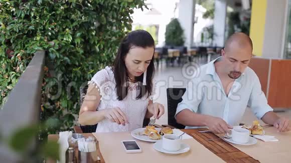 年轻夫妇在户外咖啡馆的一张桌子上吃早餐和聊天视频的预览图