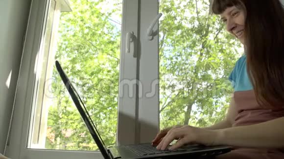 那个女人在窗台上的笔记本电脑后面工作和交流视频的预览图