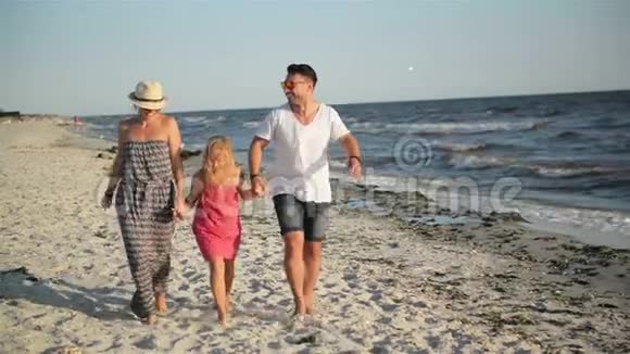 快乐的一家人和小女儿在海滩上散步在海边的暑假里牵手视频的预览图