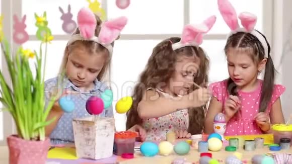 快乐的孩子们在复活节穿着兔子耳朵画鸡蛋视频的预览图
