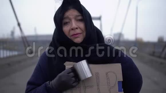 在寒冷多风灰色的天气里老乞丐在桥上请求施舍和帮助视频的预览图