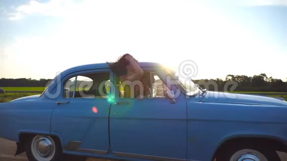 戴墨镜的快乐女孩斜倚在复古车窗外享受旅行年轻女子望着窗外移动的老人视频的预览图