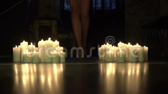 优雅的女人光着腿在黑暗的房间里的蜡烛之间向前走视频的预览图