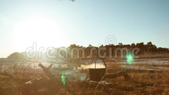 剪影点燃篝火徒步旅行者停在露营地徒步旅行者水壶里的水沸腾在夕阳的剪影中点燃阳光视频的预览图