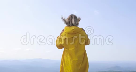 穿着黄色雨衣的女人在山顶上年轻女性健康活跃的生活方式在大自然中冒险视频的预览图
