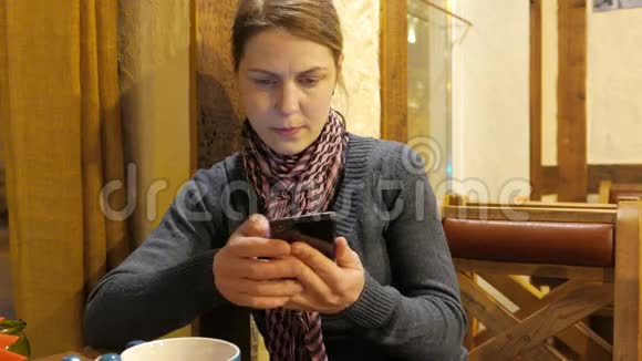 年轻的女人在手机上使用应用程序喝咖啡在咖啡馆里微笑4UHDK视频的预览图