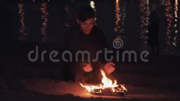 年轻的旅行者坐在海边沙滩上燃烧的鞋子篝火旁视频的预览图