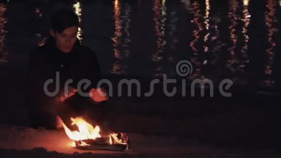年轻的旅行者坐在海边沙滩上燃烧的鞋子篝火旁视频的预览图