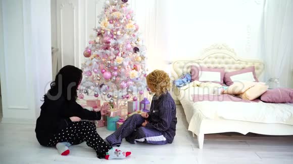 两位亲密的朋友分享愉快的情感和节日礼物坐在床边明亮的卧室和圣诞节的地板上视频的预览图