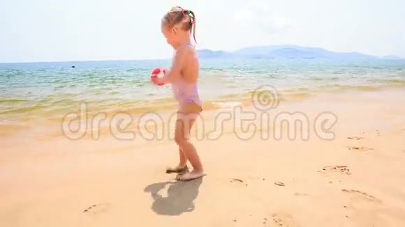 浅海沙滩上的金发小女孩带着球跑视频的预览图