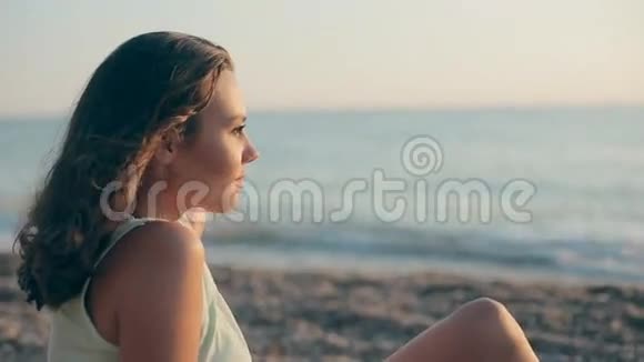 快乐的女孩坐在海边的鹅卵石上若有所思地向远方望去视频的预览图