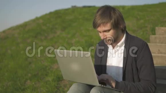 青年坐在公园楼梯上的笔记本电脑画像视频的预览图