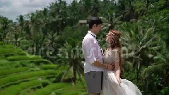 新婚夫妇在巴厘岛的米台上摆姿势牵手拥抱浪漫的婚礼视频的预览图