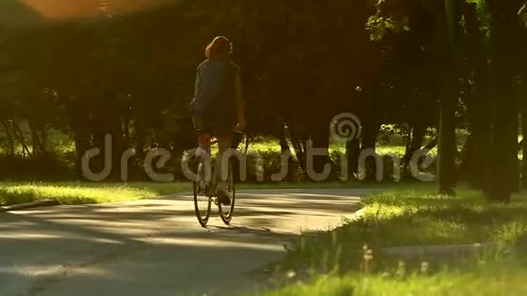 女人开始骑自行车穿过一个绿色的草地公园在树木和日落上视频的预览图