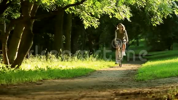 女人开始骑自行车穿过一个绿色的草地公园在树木和日落上视频的预览图