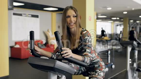 漂亮的女人在健身房骑自行车骑自行车阳光健身房视频的预览图