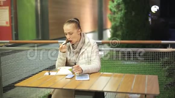 一位中年白人妇女在一个寒冷的夜晚坐在一家夏季咖啡馆的桌子旁吃蔬菜沙拉和油炸食品视频的预览图